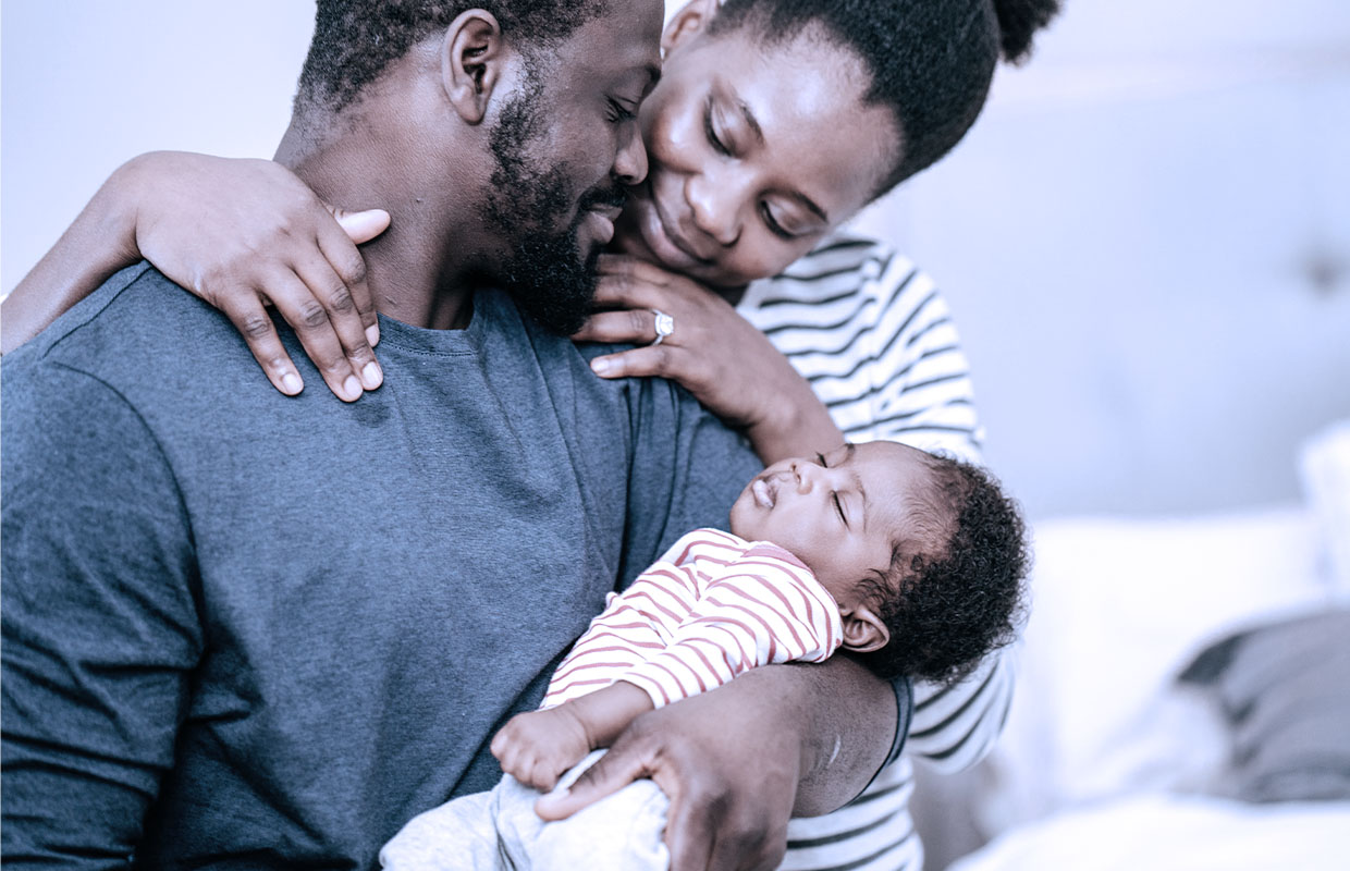 Mother hugs father who is holding his newborn baby girl in their home.