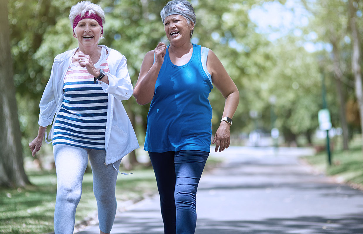 two senior ladies walking briskly on a trail laughing