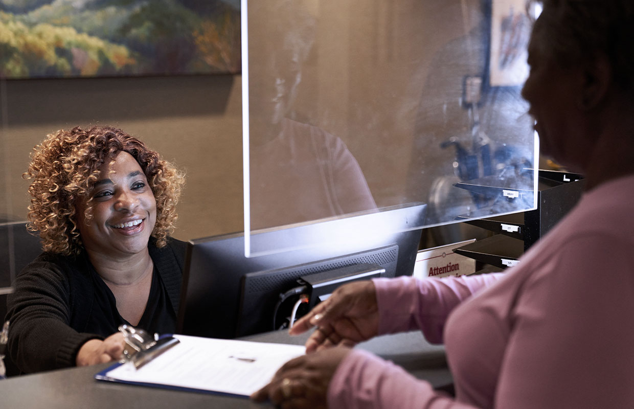 young female at registration desk handing paperwork to female patient