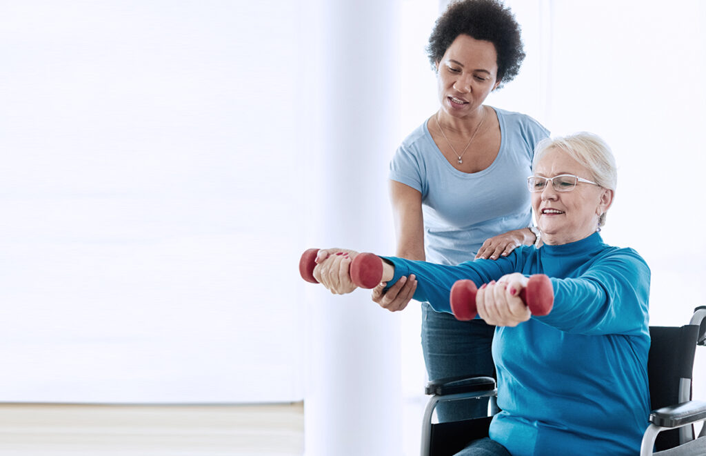 young female physical therapist helping elderly female lift weights