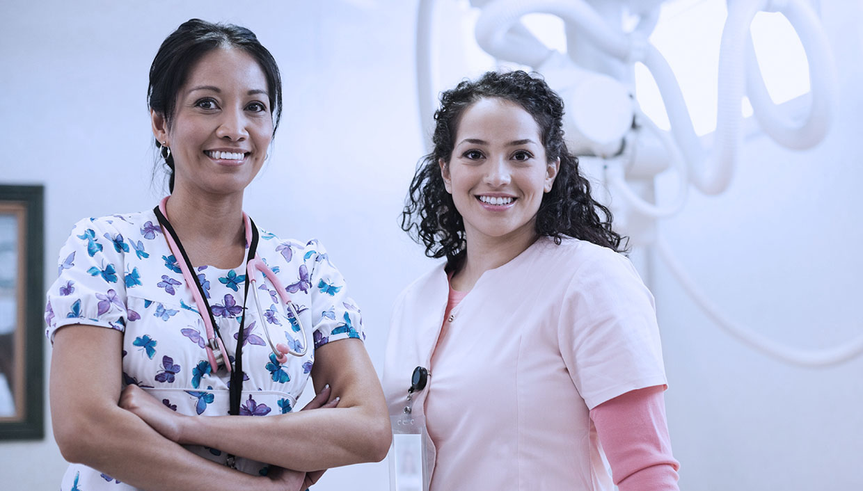 Two mammography techs stand in tomosynthesis breast screening clinic.