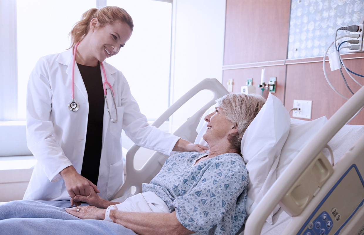 young female doctor comforting elderly female patient in a hospital bed