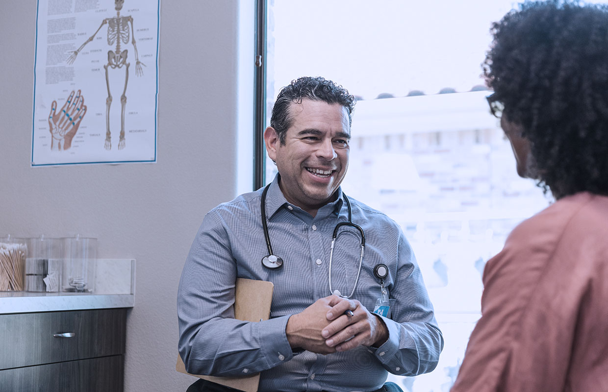 Male physician talks with female patient in an exam room.