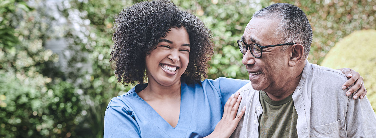 a nurse assists an elderly man walking outside in a park