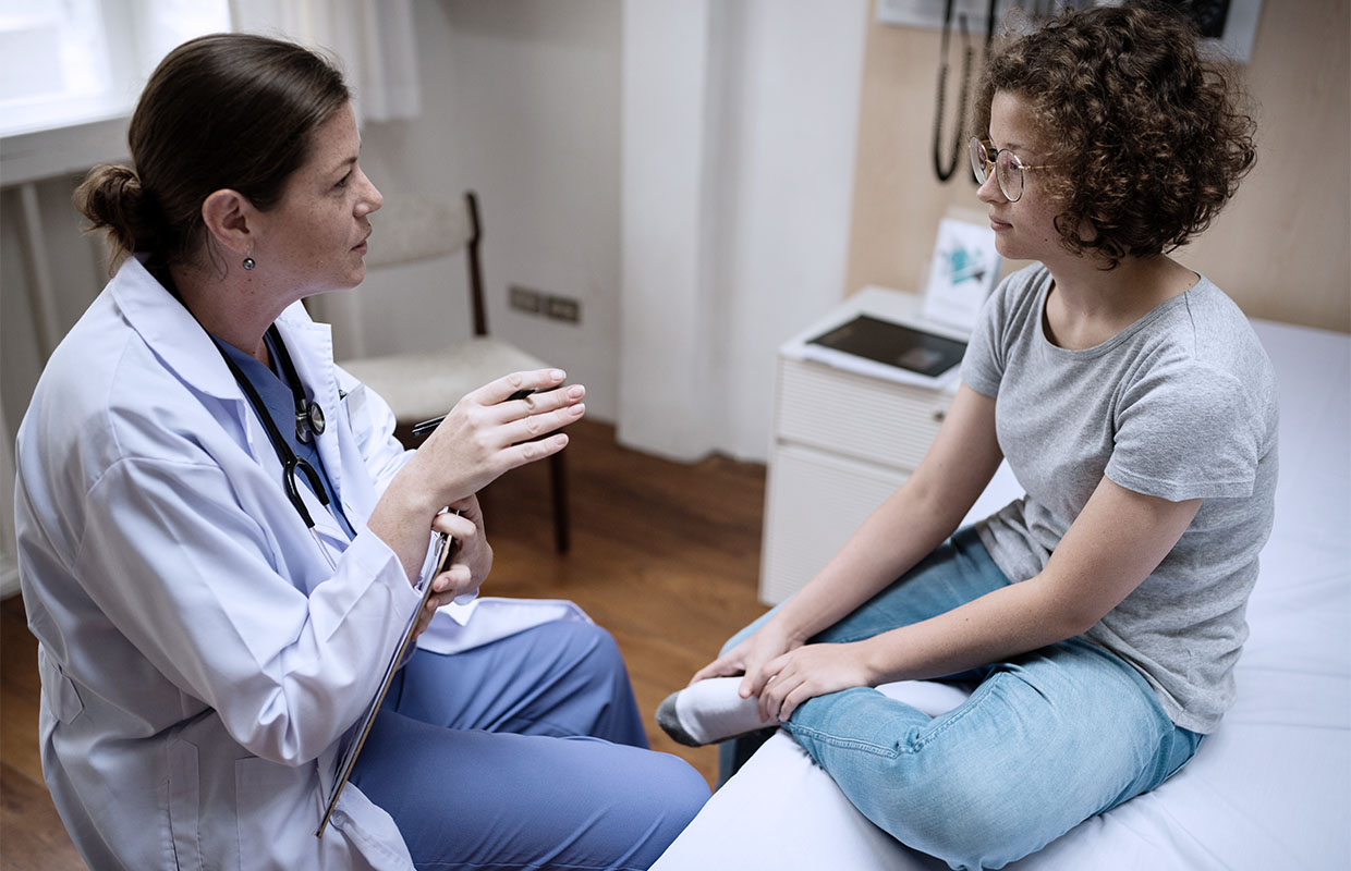 middle age female doctor talking to teenage girl sitting on a bed