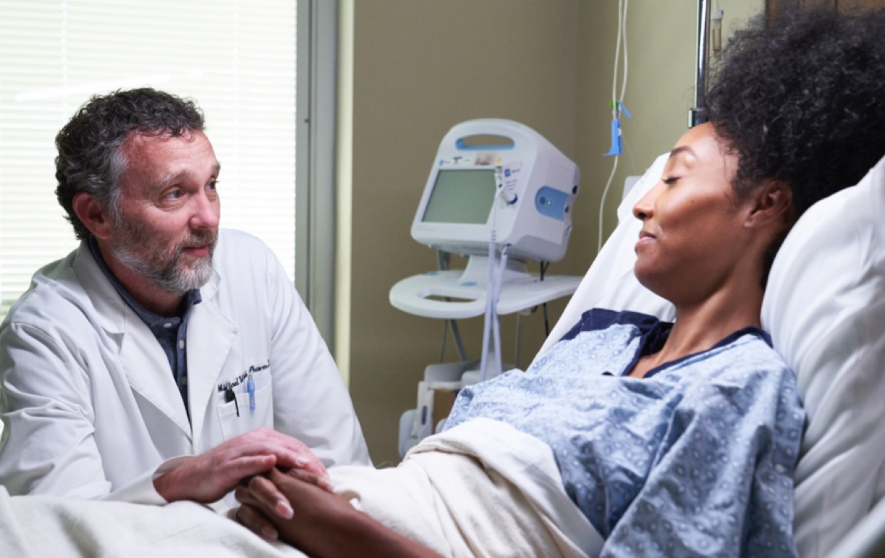 A male doctor comforting a patient who's in a hospital bed recovering.