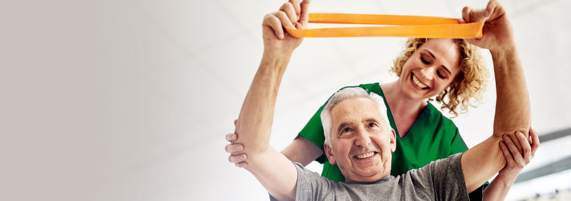 young female therapist helping an elderly male patient stretch a resistance band above his head