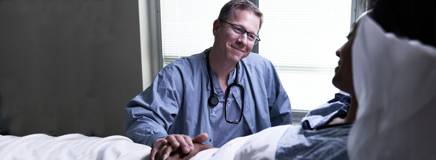 middle age male doctor in scrubs talking to a patient in bed