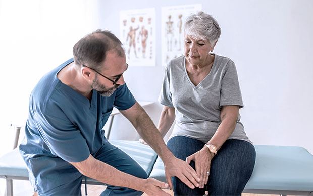 male doctor in scrubs examining the knee of a senior female patient