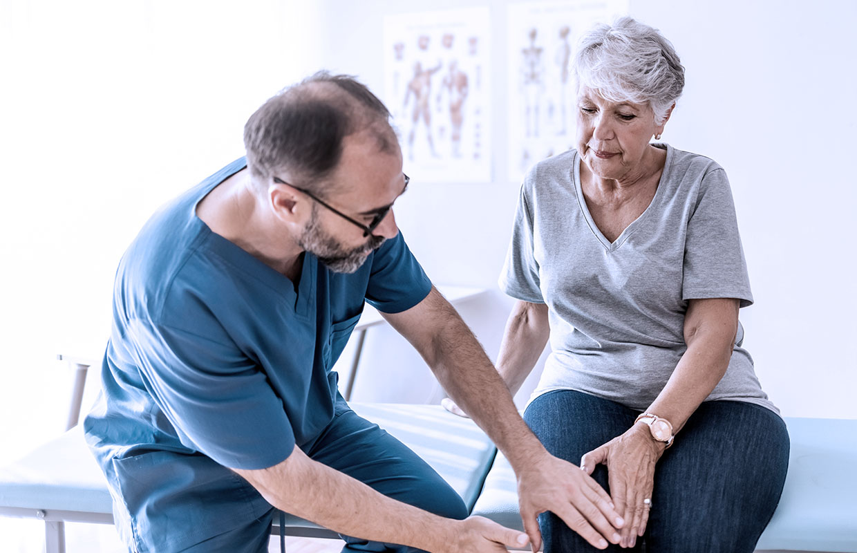 male doctor in scrubs examining knee of senior female patient