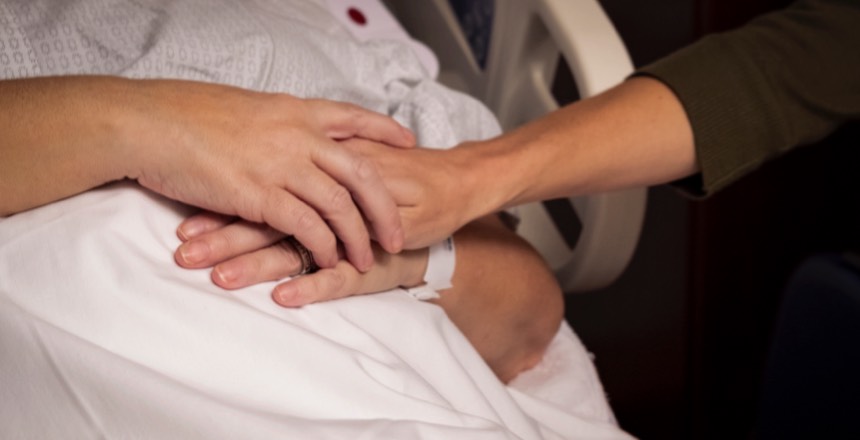 someone holding the hand of a patient in a hospital bed