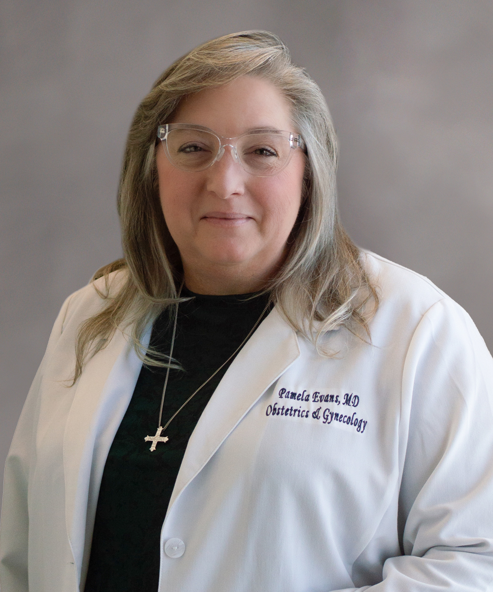 A woman with long, light brown hair and glasses wears a white lab coat labeled Pamela Evans, MD Obstetrics & Gynecology—serving labor and delivery in Morristown—and a cross necklace, standing against a neutral gray background.