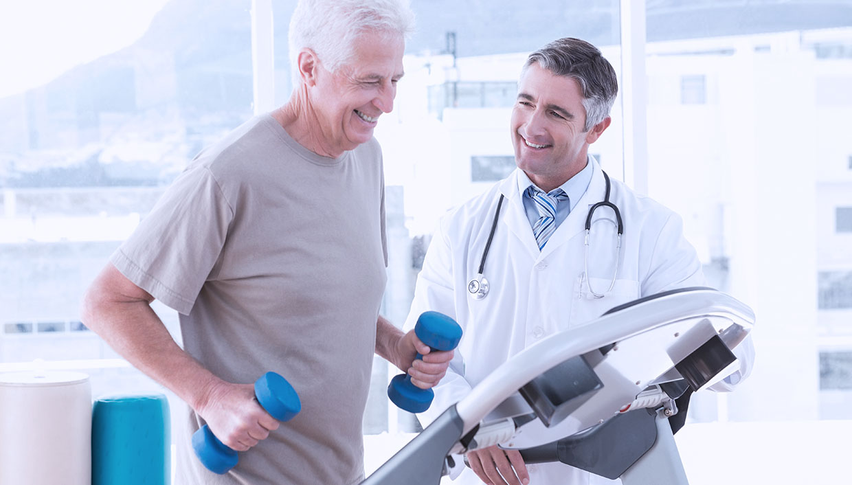 senior male patient exercises on treadmill while holding weights as senior male doctor observes