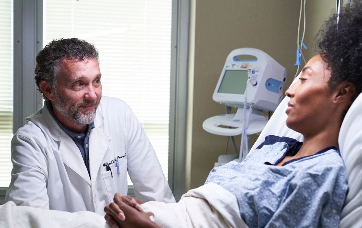 middle age male doctor holding hand of female patient in hospital bed