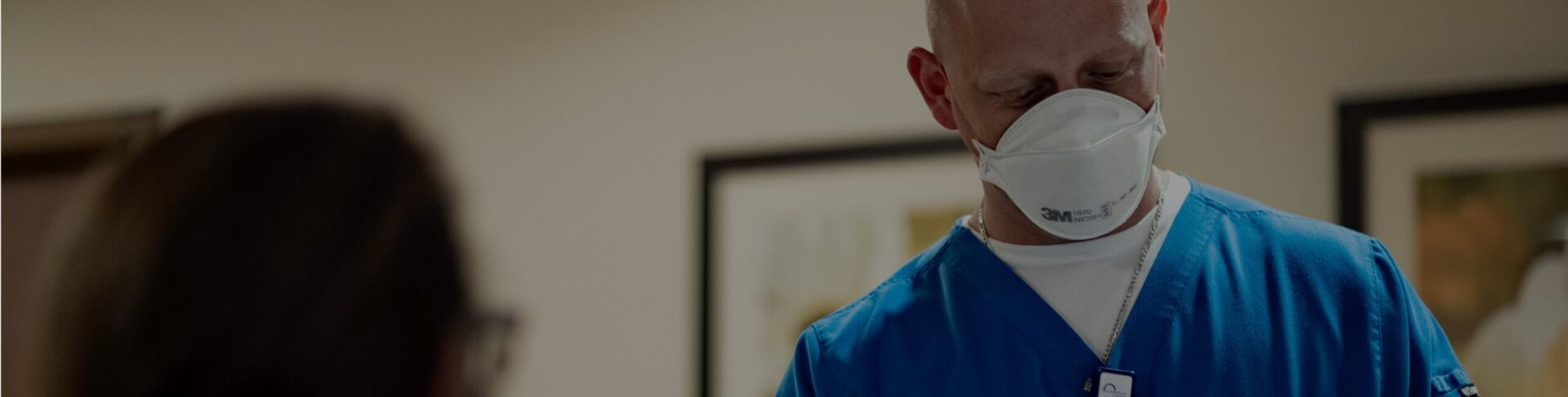 male nurse in blue scrubs and mask at registration desk at covenant health