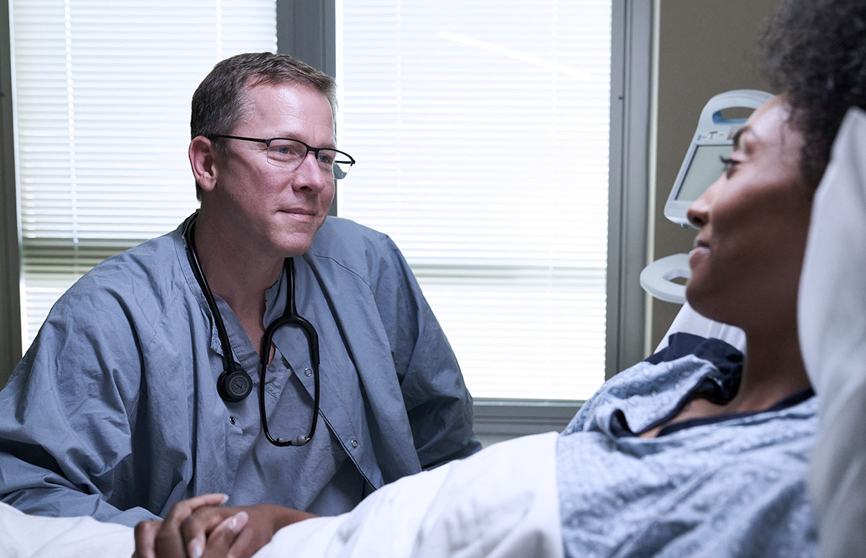 male doctor holding the hand of female patient in hospital bed