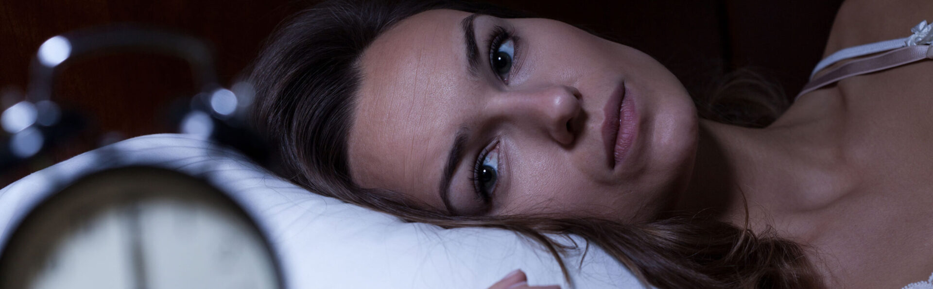 female struggling to fall asleep staring at clock in bed