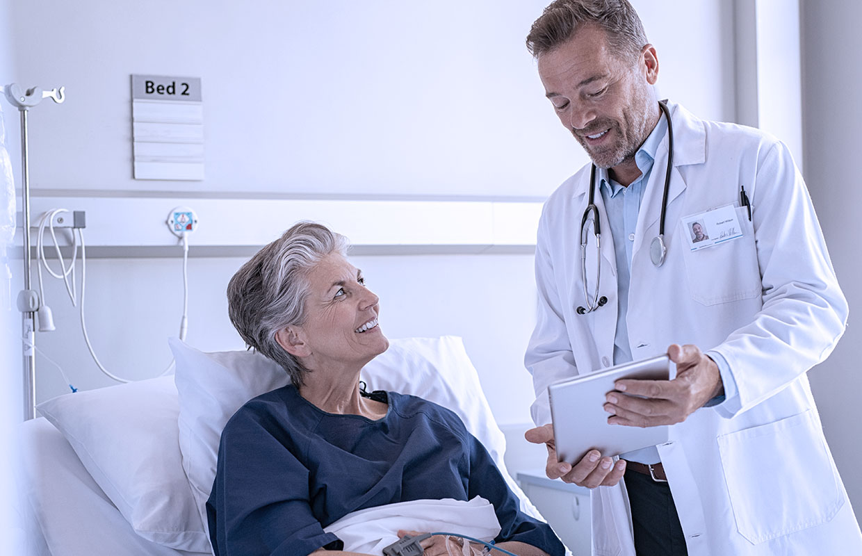 senior female patient in bed talking to middle-aged male doctor