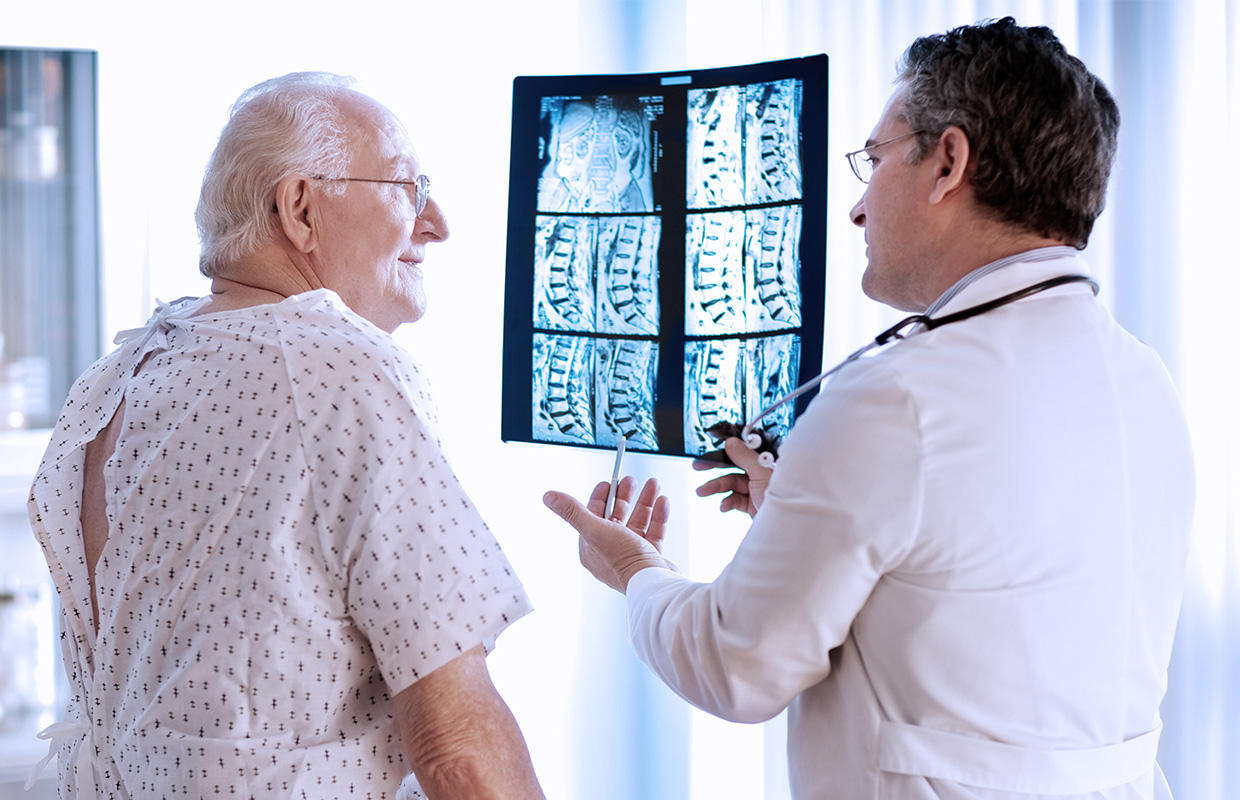 elderly man looks at middle aged male doctor showing spine xrays