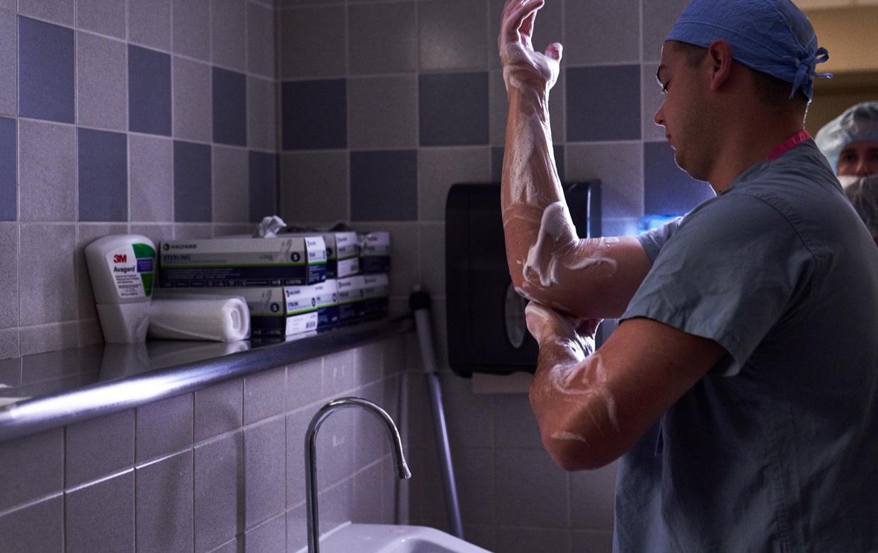male surgeon in scrubs washing hands and arms