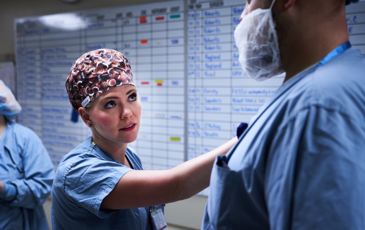 female surgeon talks to male surgeon with schedule board
