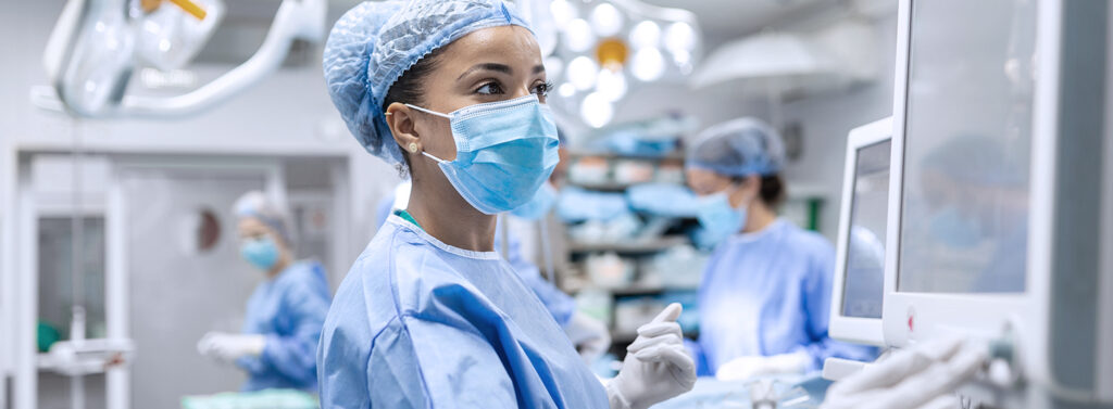 female surgeon in scrubs and mask looking at computer in operating room