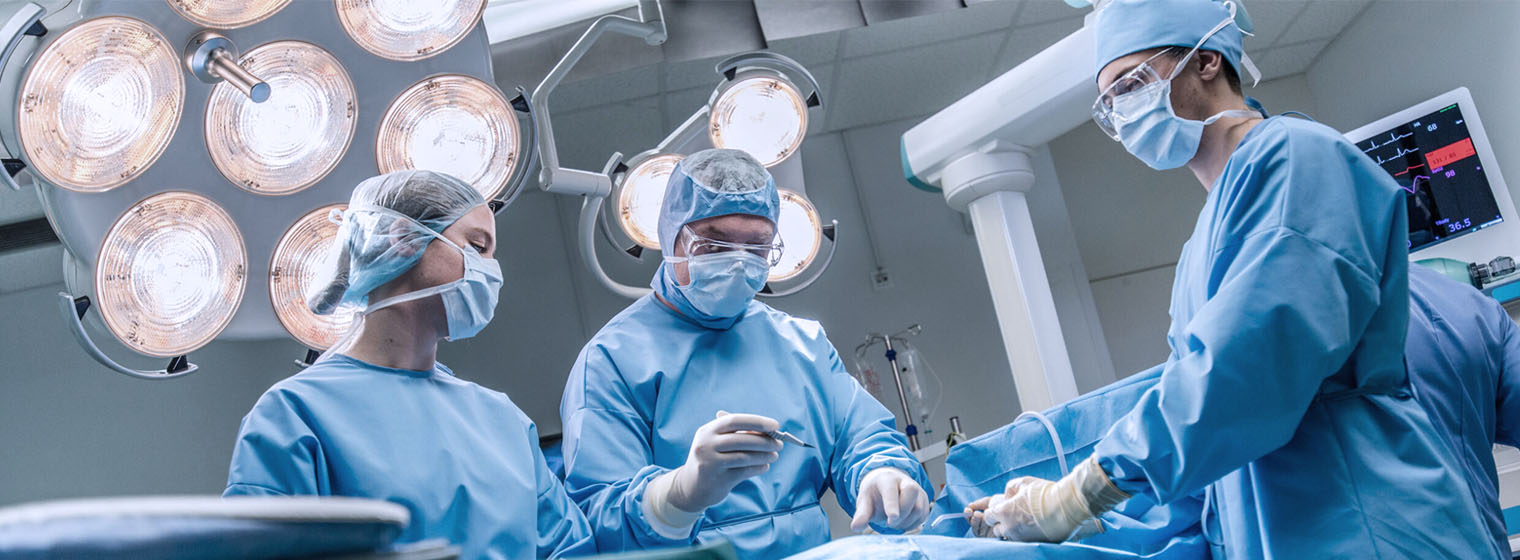 three surgeons in blue scrubs in surgical suite