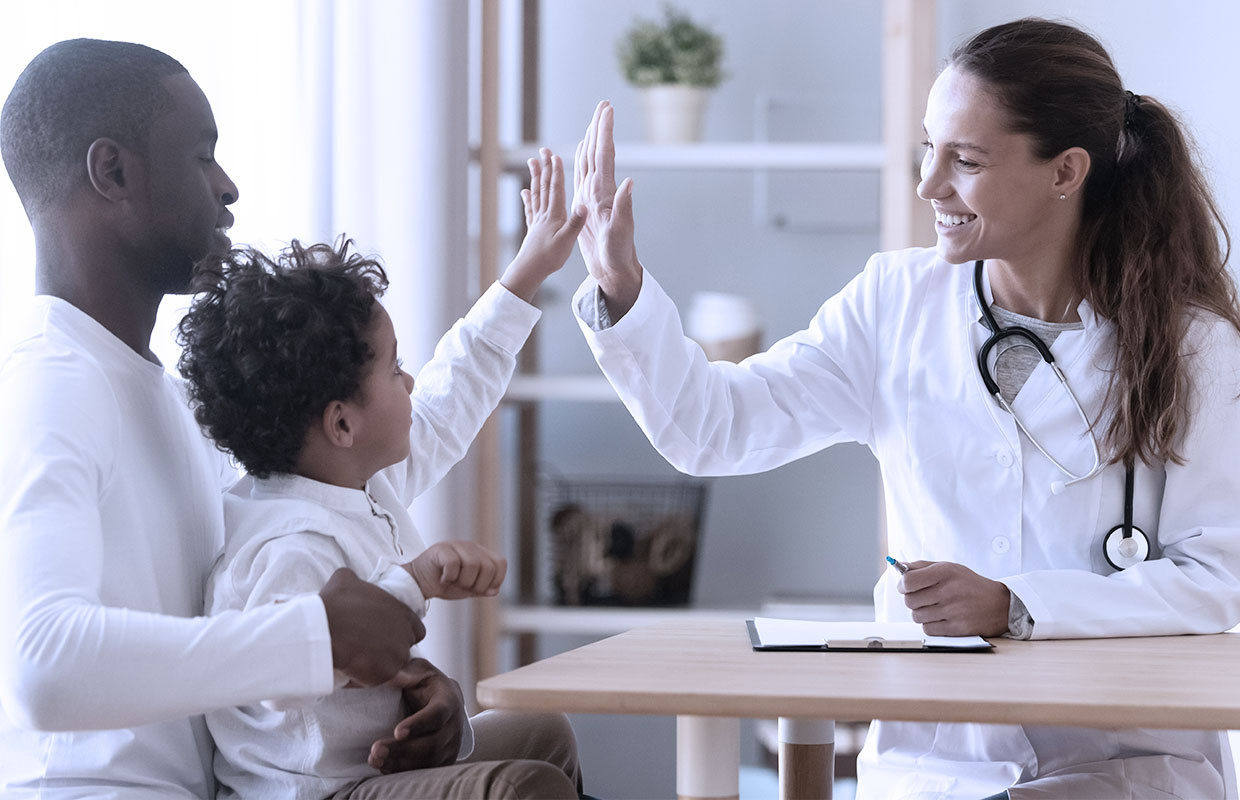 female doctor high fives young child sitting on father's lap