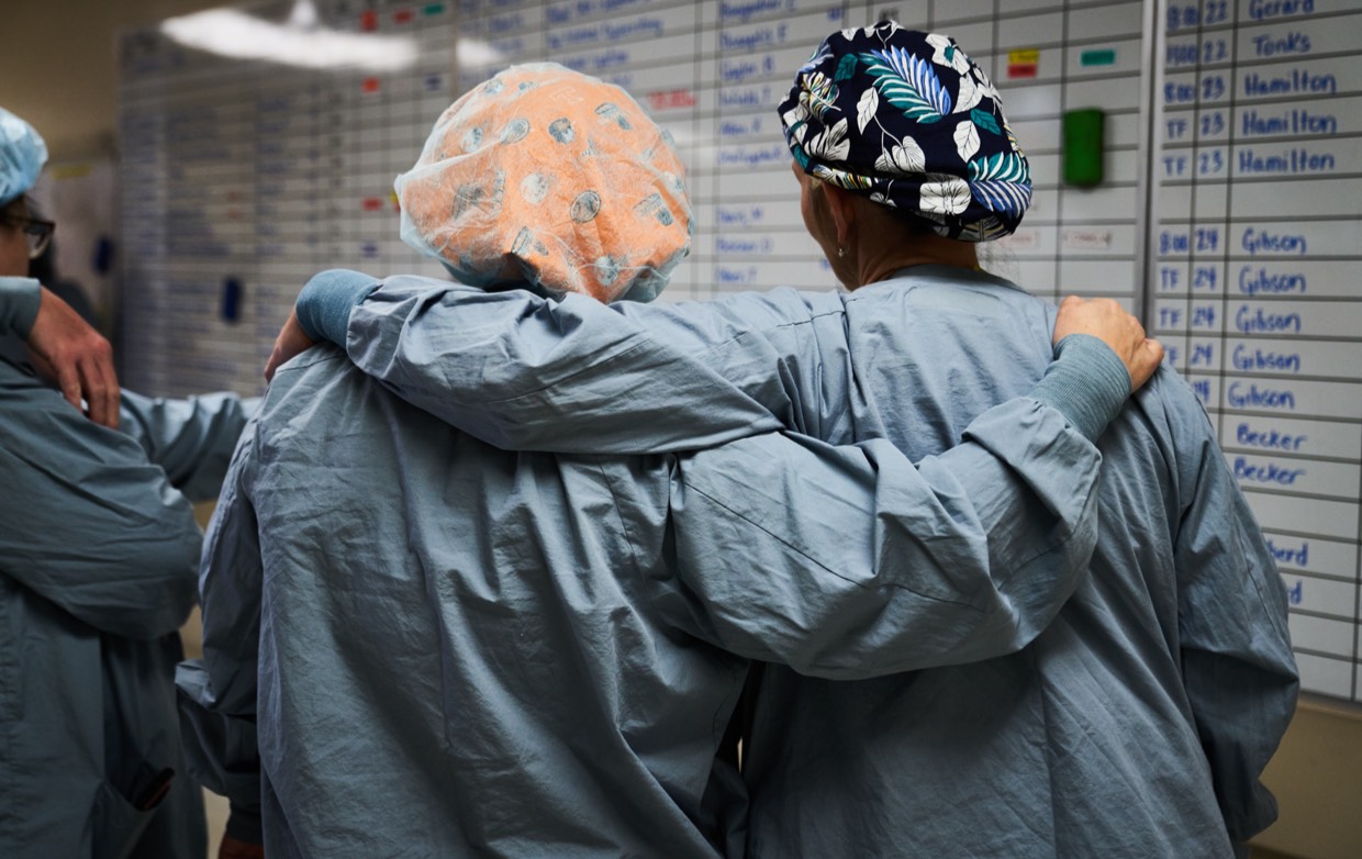 two surgeons with arms around each other looking at surgery schedule board