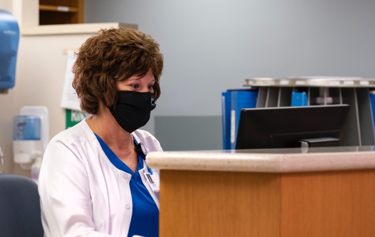 older female nurse in mask sitting at a registration desk