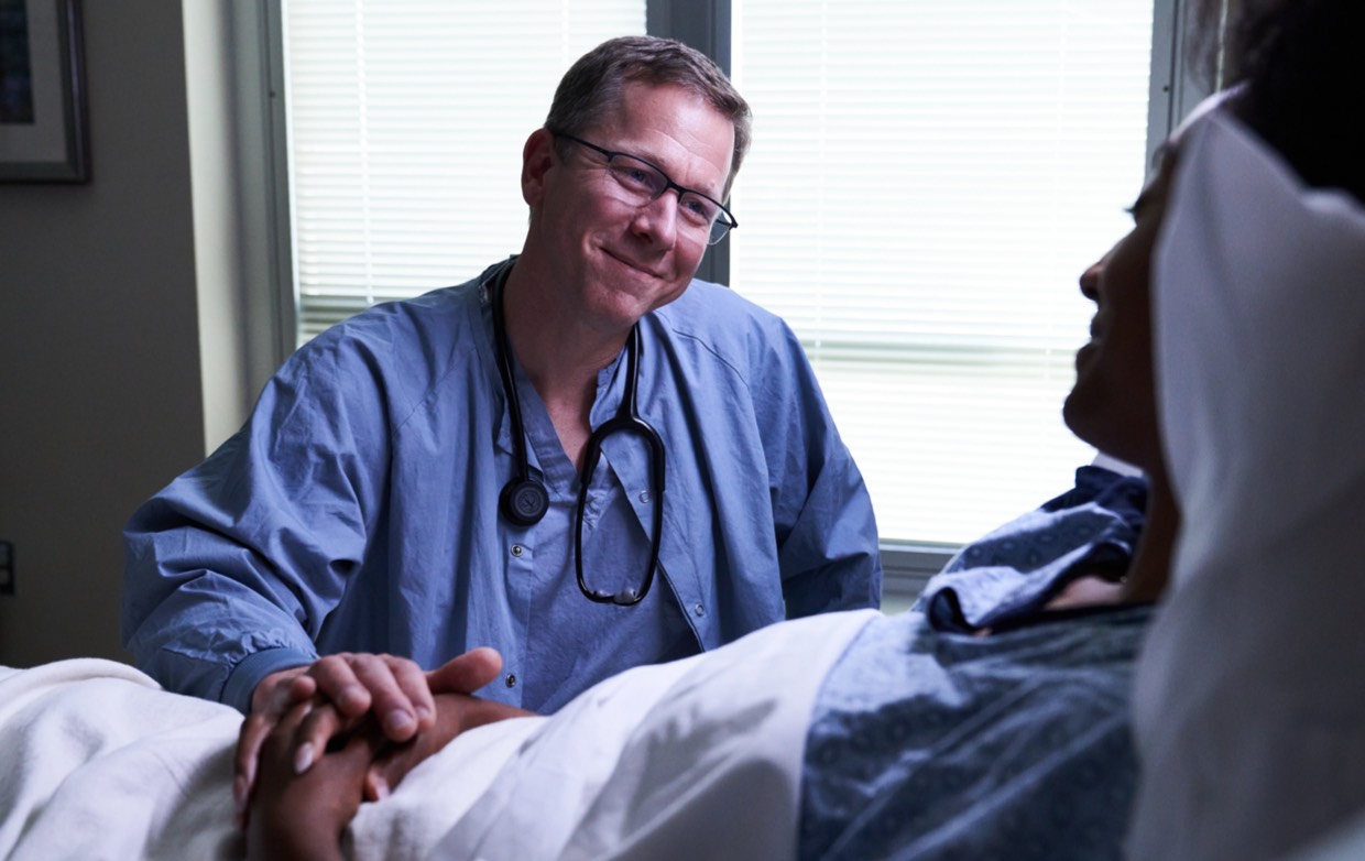 male nurse in scrubs holding hand of female patient in hospital bed