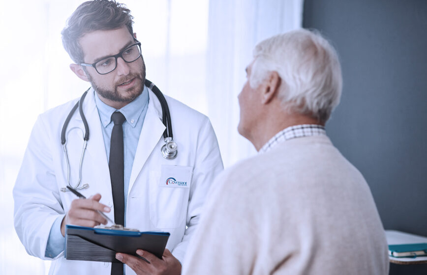 male doctor with stethoscope and clipboard talking to elderly male patient