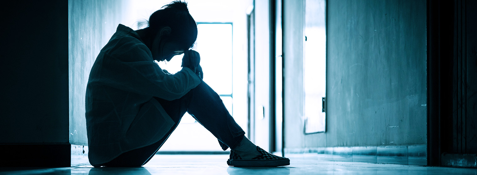 a woman sits in a dark hallway and rests her head on her knees