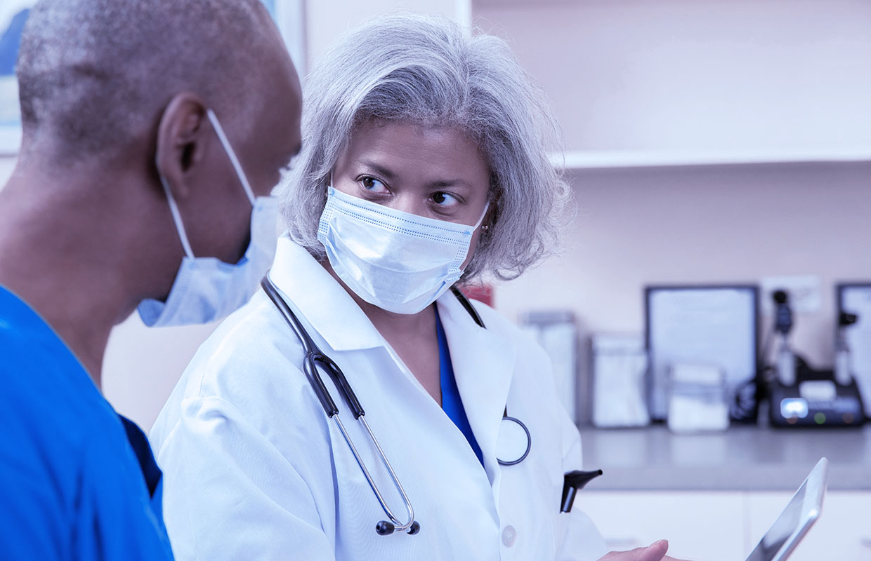 A doctor and a nurse stand in an exam room and talk about something on an ipad