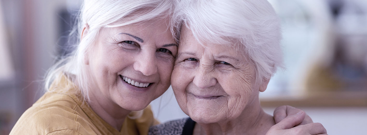 two elderly women smile and pose for a photo