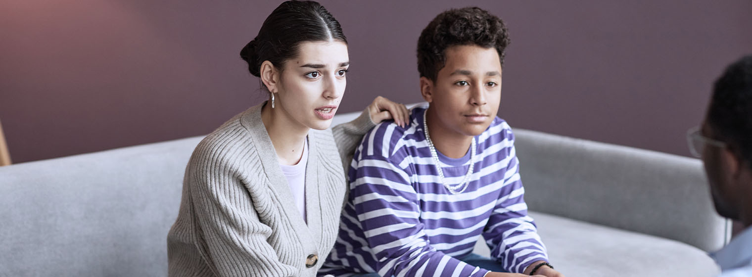 teenage boy sitting on couch with concerned mother talking to a therapist