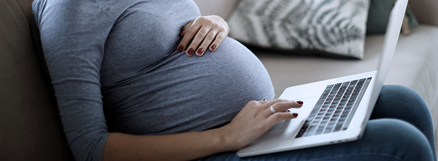 a pregnant woman on a laptop computer while sitting on the couch