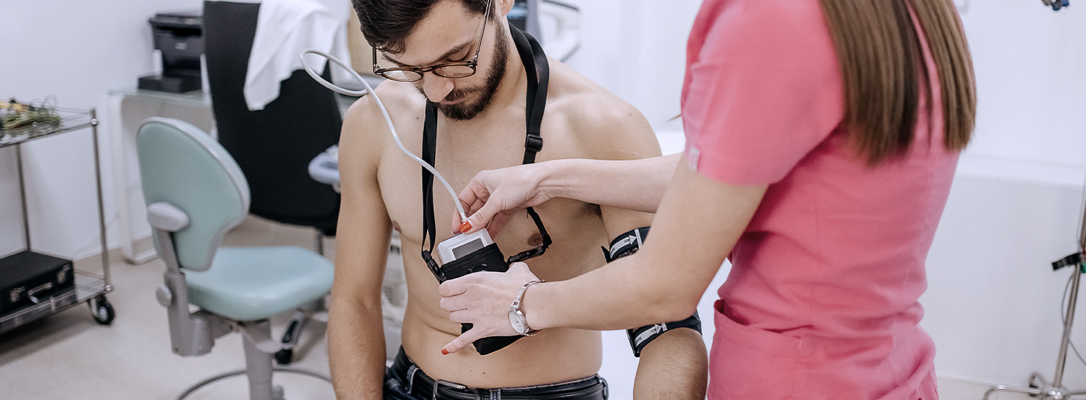 female nurse in pink scrubs attaching holter monitor to shirtless male