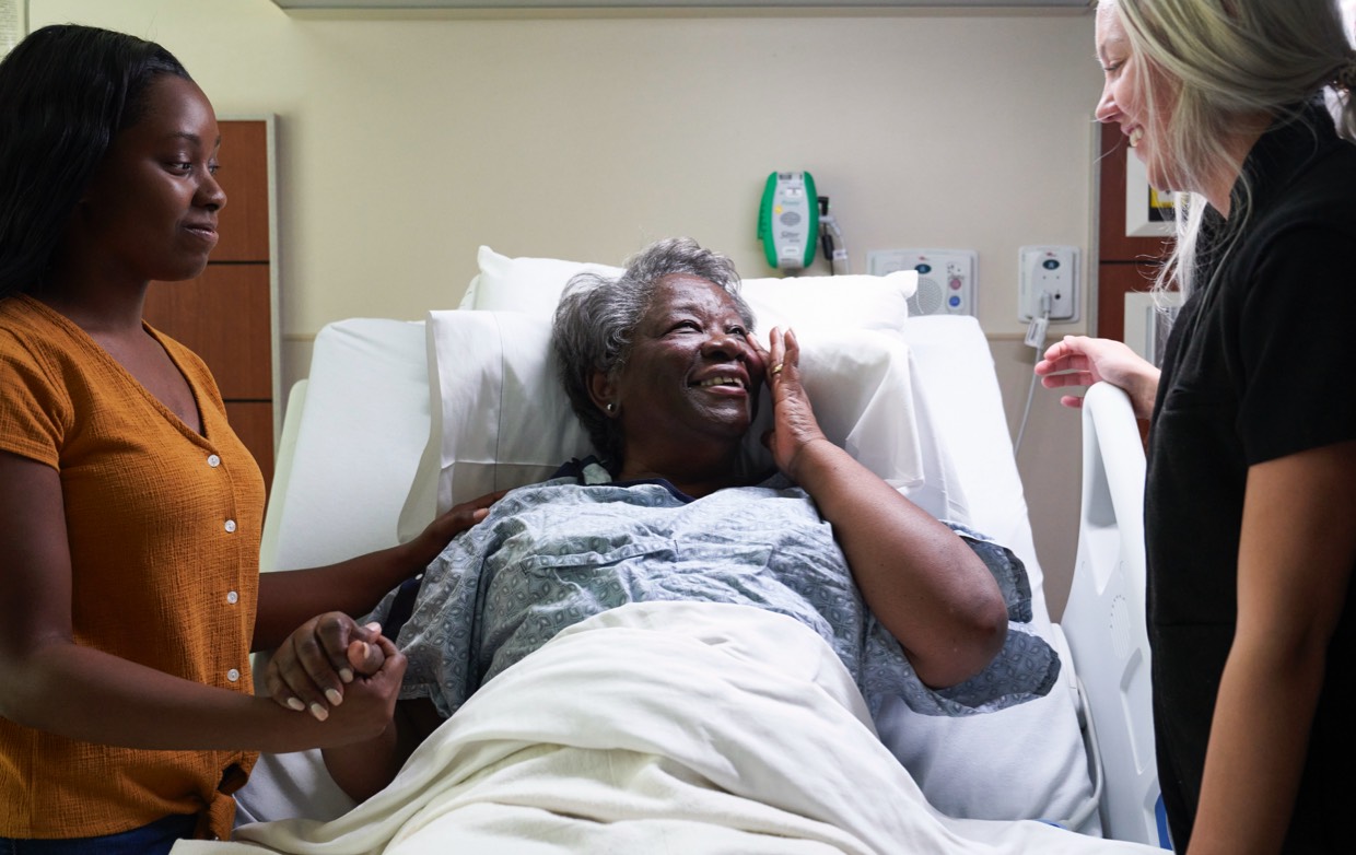 A patient with a female family member smiling up to a nurse.