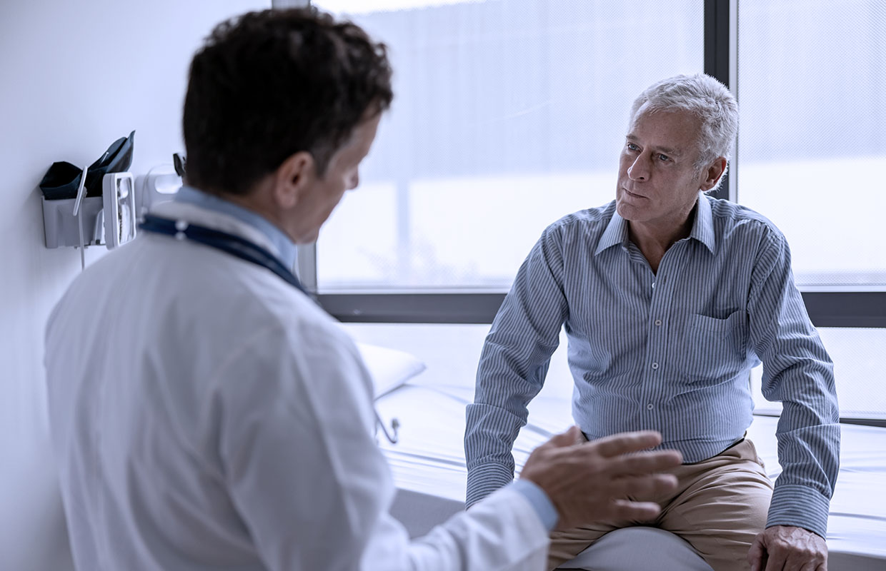 doctor talks to man in exam room while he sits on table