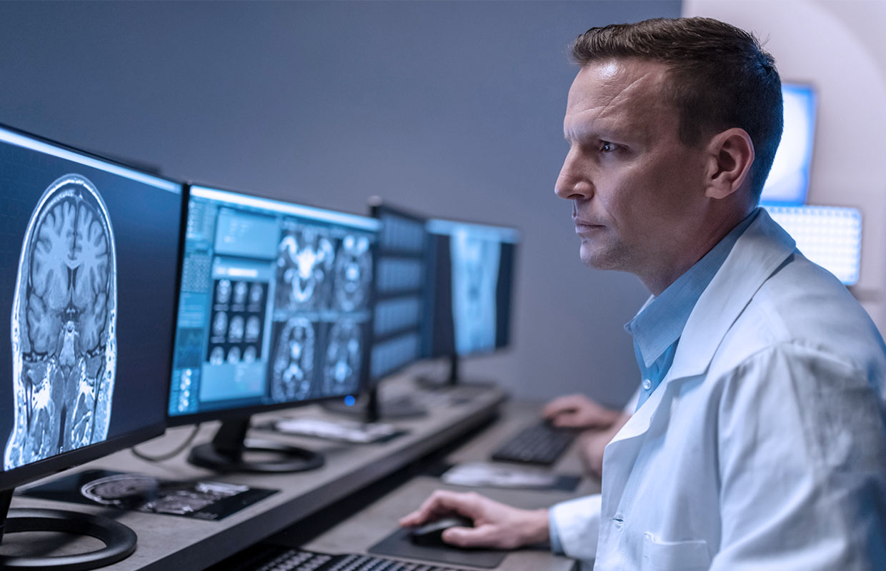 a doctor sits in front of a computer and reviews mri images on the screen