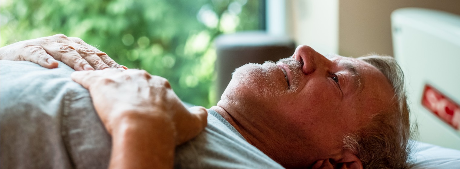 Man laying down on a table with hands on his chest to be examined
