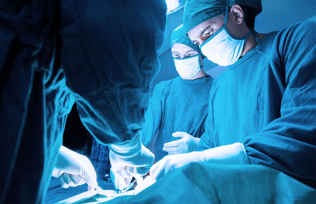 a group of surgeons perform a surgery while huddled over a patient