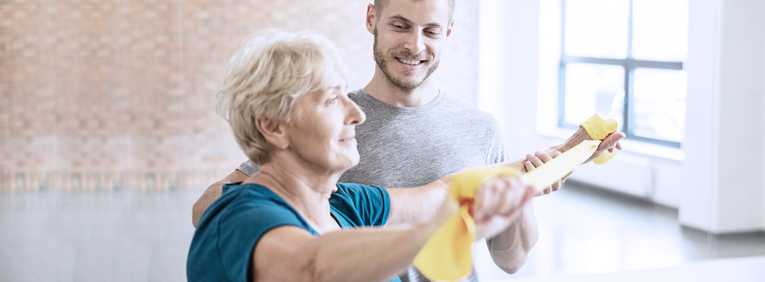 Male physical therapist guides older female through strengthening exercises