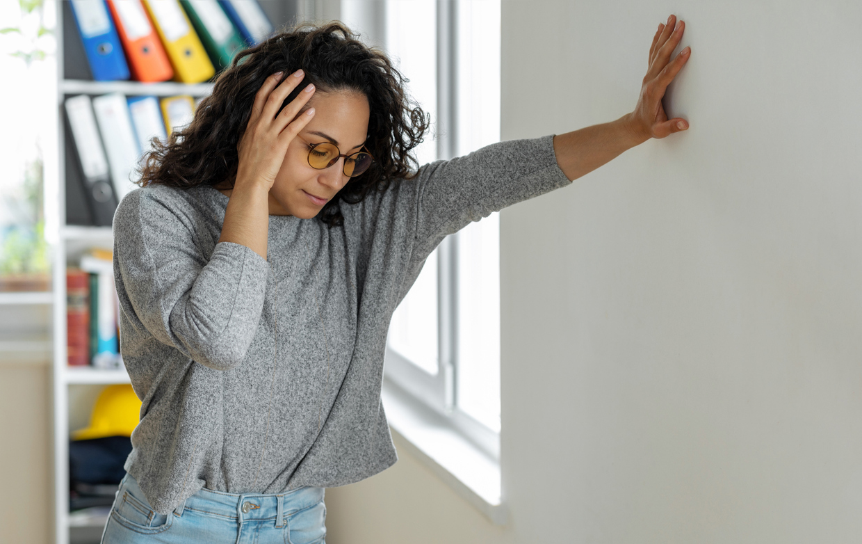 Woman leaning on wall with one hand on head with vertigo