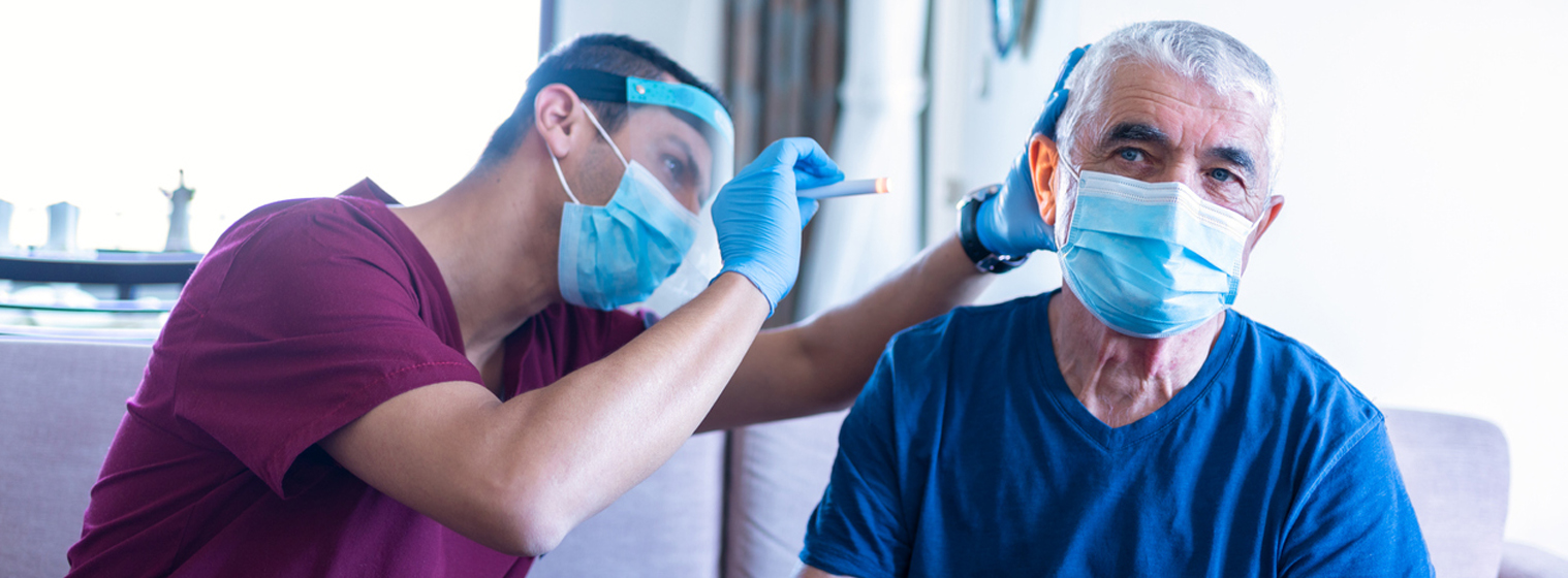 male medical professional using light to look into elderly man's ear