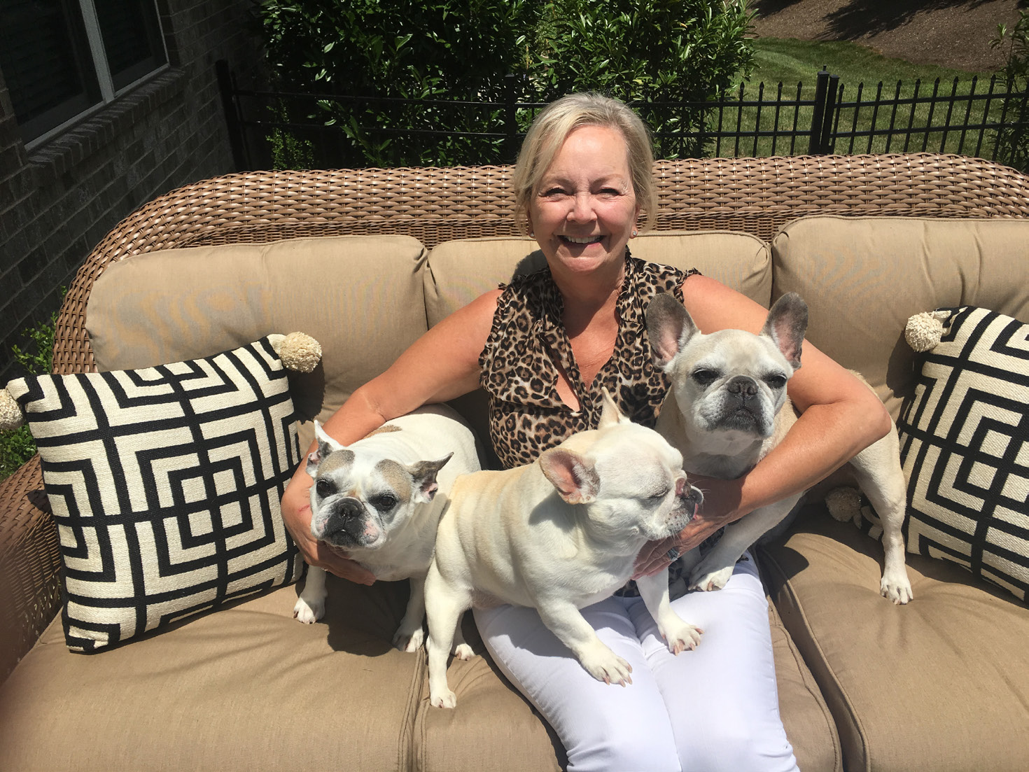 Deb Bunner sitting on outside couch with 3 french bulldogs