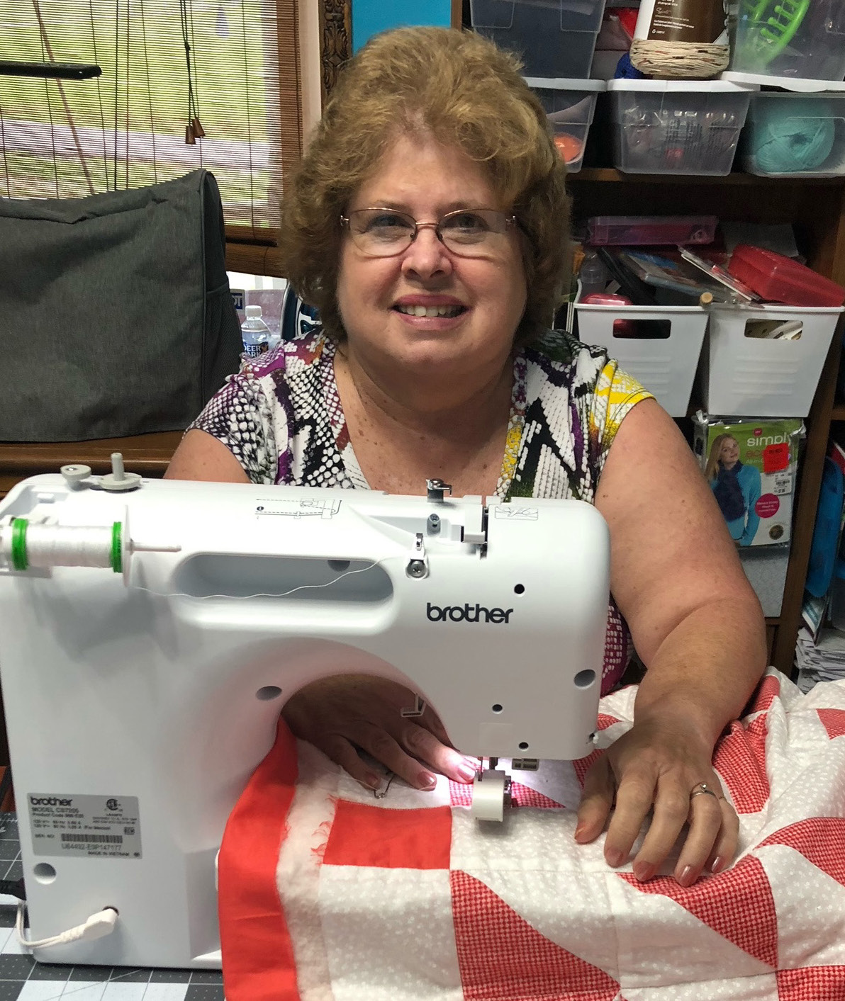 Freida Rogers sits behind her sewing machine smiling.