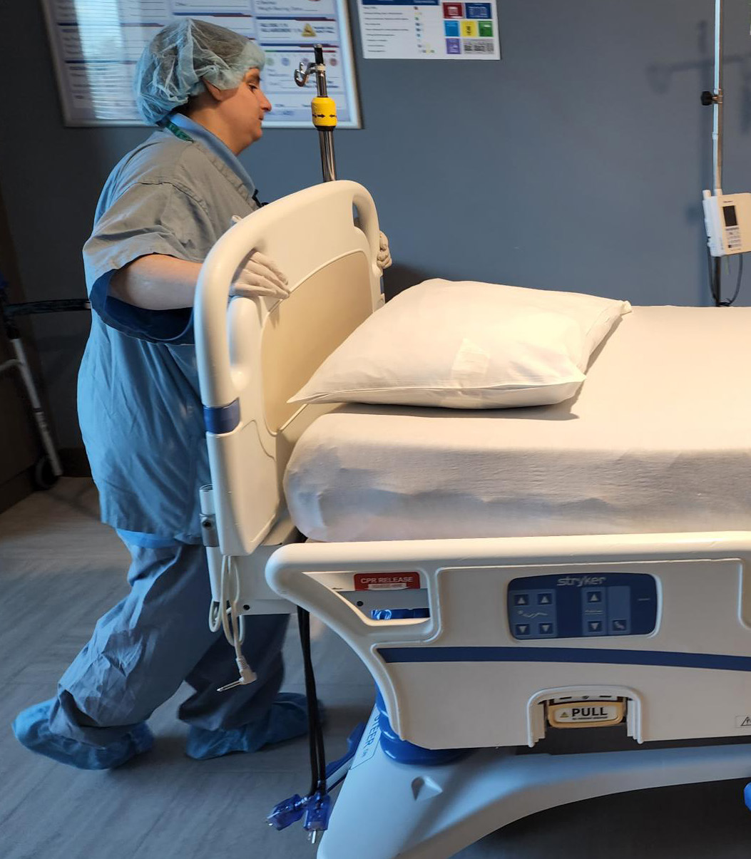 Ashley in surgical scrubs pushing bed through hallway.