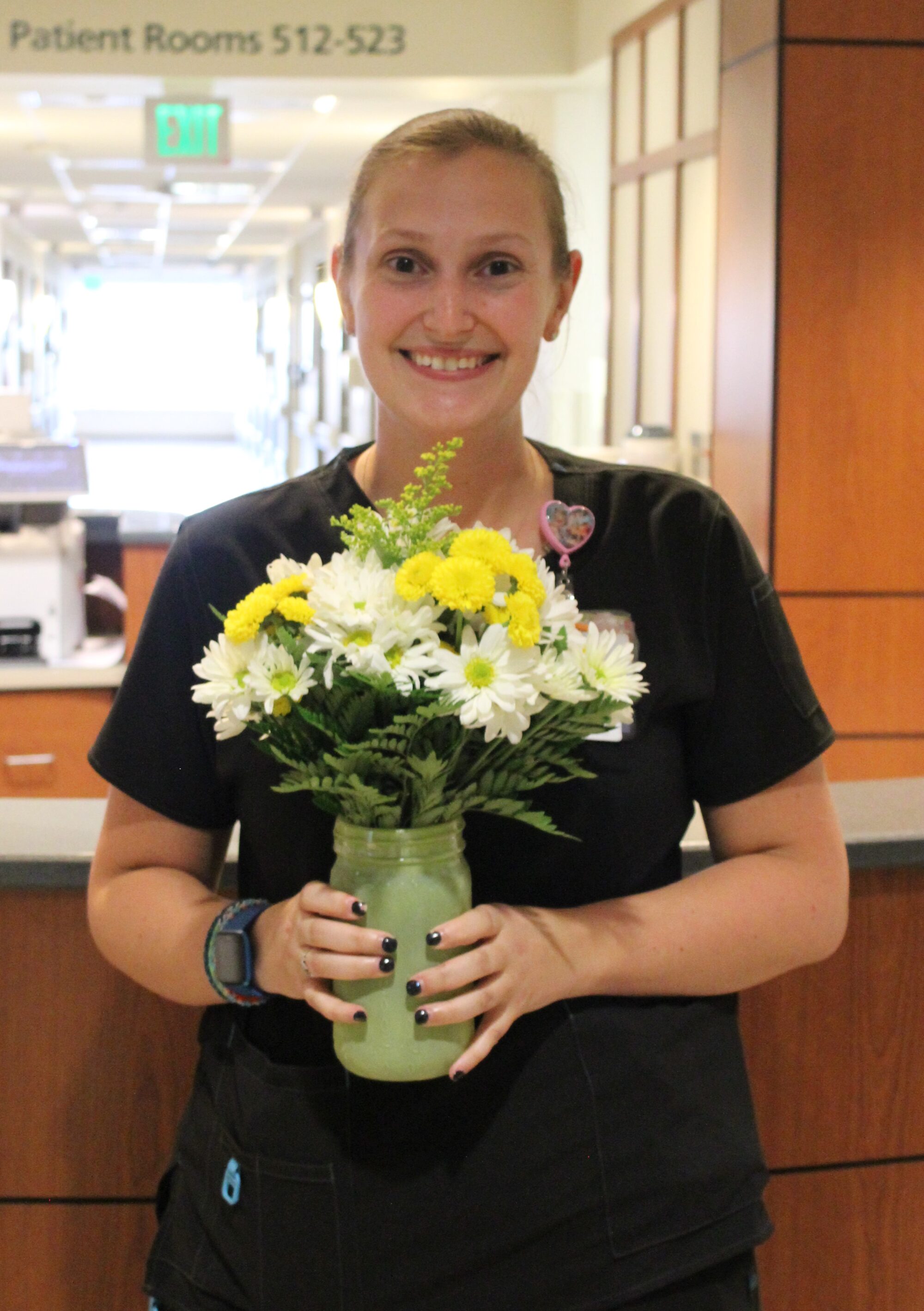 Anne wearing black scrubs and holding arrangement of yellow and white daisies.